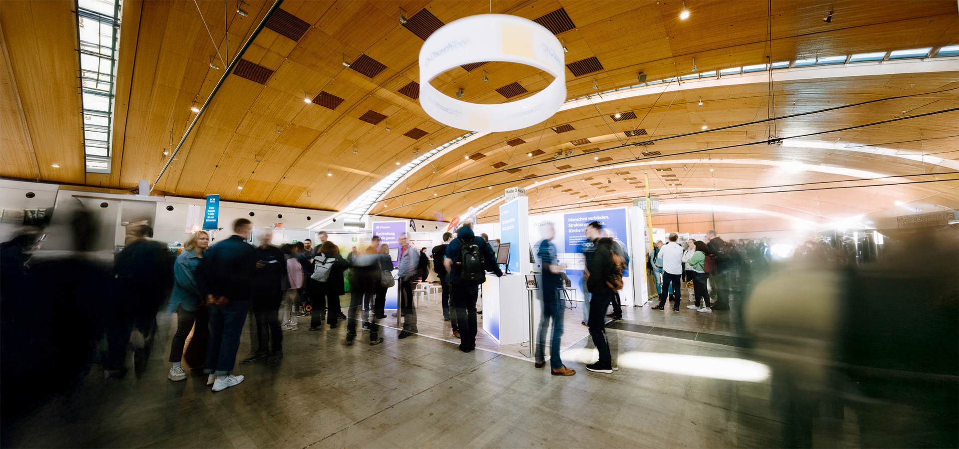 Vibrante Messehalle mit moderner Holzdecke, lebhaften Besucherstrom und Ausstellerständen – N3W-Messeservice unterstützt Aussteller bei der professionellen Planung und Umsetzung ihres Messeauftritts.