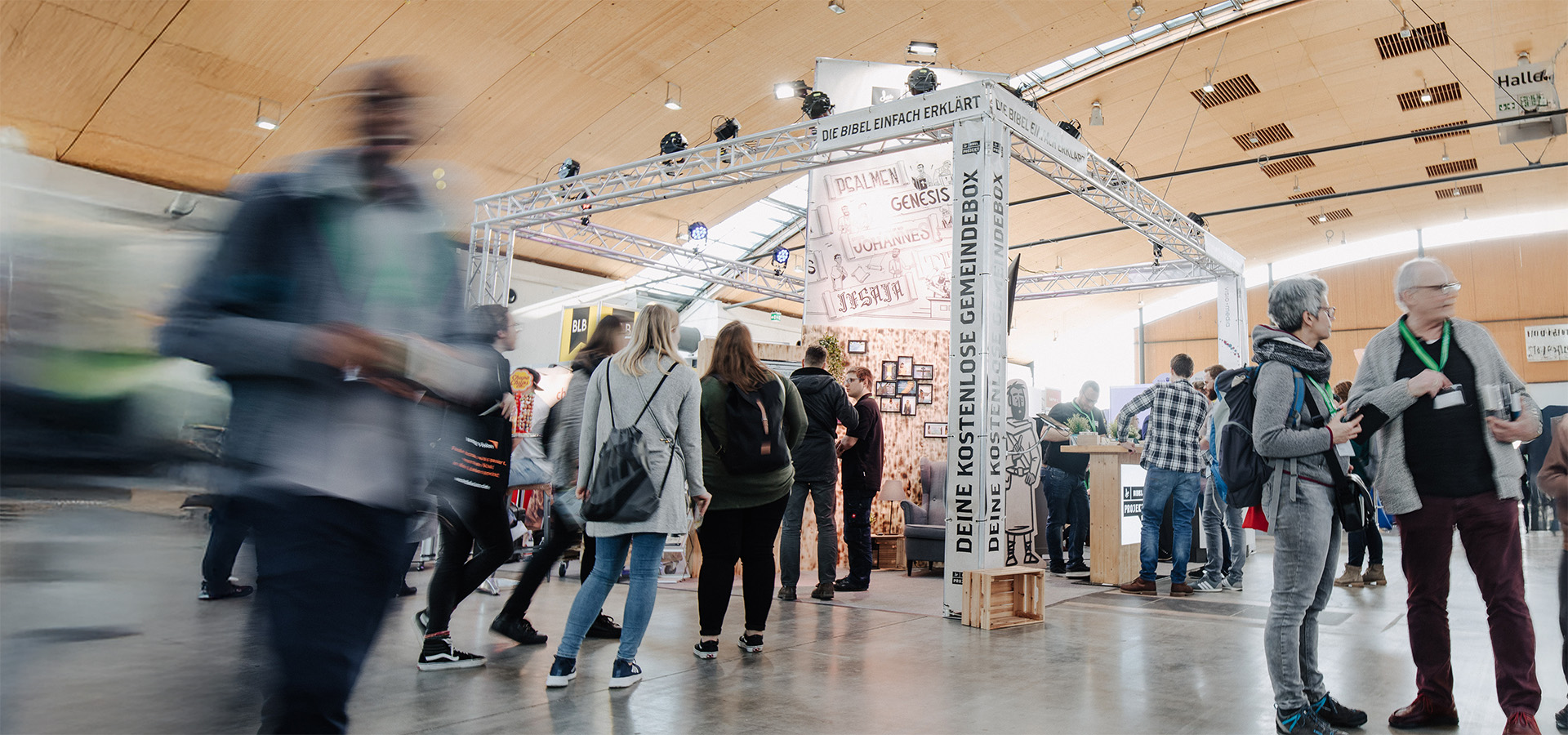 Ein belebter Messestand auf einer Convention, mit einem Stand, der die Schilder „Die Bibel einfach erklärt“ und „Deine kostenlose Gemeindebox“ trägt, wo Besucher mit Ausstellern interagieren. Dieses Bild veranschaulicht die Rolle von N3W-Messeservice bei der Unterstützung professioneller Messeauftritte.